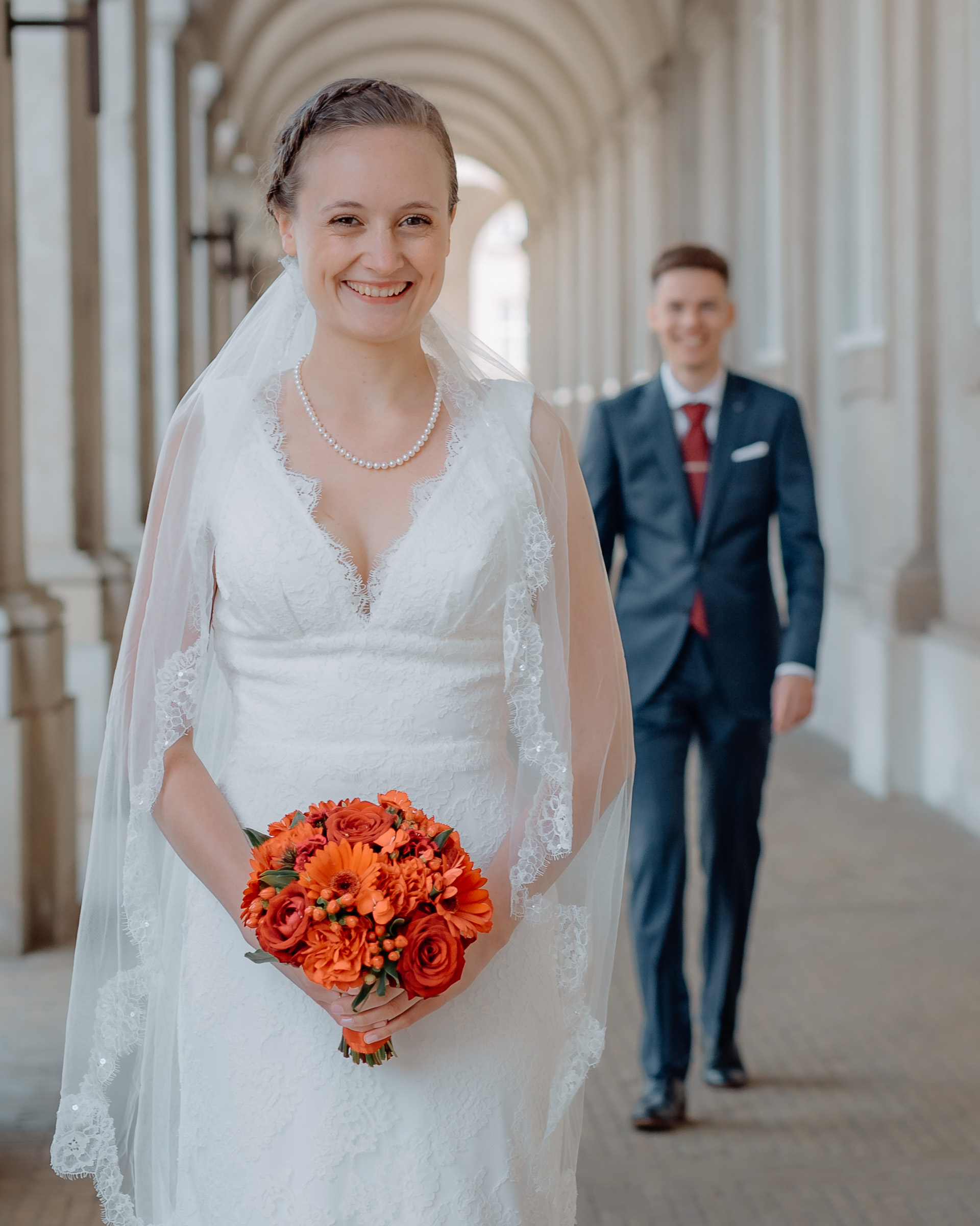 Brud i elegant arkade med brudgom i baggrunden